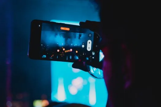 Smartphone screens showing blurred social media reactions to a concert controversy on a desk, neutral newsroom lighting