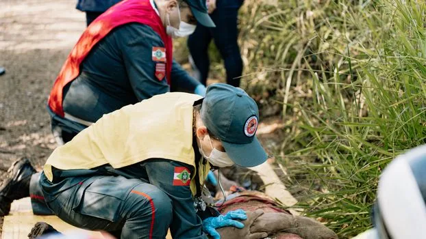 emergency heat illness first aid scene in Korea, person resting in shade while coworker calls 119 and cools neck with towel, realistic non-graphic photo, no logos