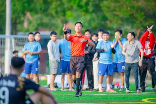Korean football fan checking Vietnam Cambodia match schedule on phone near television, Hanoi stadium photo on screen, evening sports viewing setup, no readable logos | 베트남 캄보디아전 시간을 휴대폰과 TV 편성표로 확인하는 장면