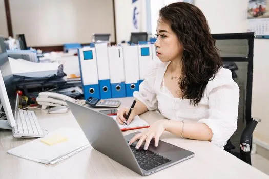Korean home buyer reviewing building register PDF on laptop with address memo and real estate contract folder, realistic daylight desk