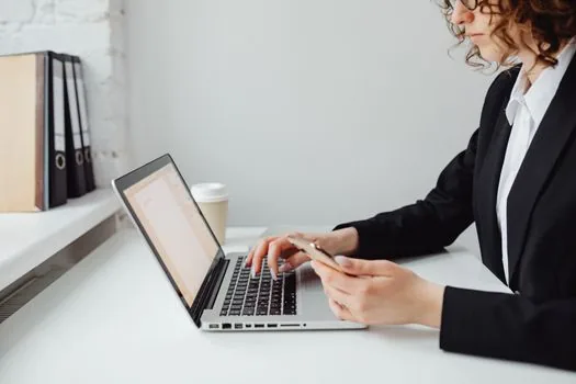 Korean person checking passport photo file properties on laptop, open passport and smartphone government application page beside it, realistic bright desk photo, no text