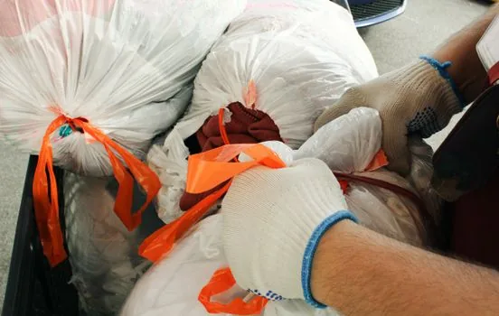Korean resident checking local volume-rate garbage bag price table on smartphone beside white trash bags and moving box, realistic apartment entrance