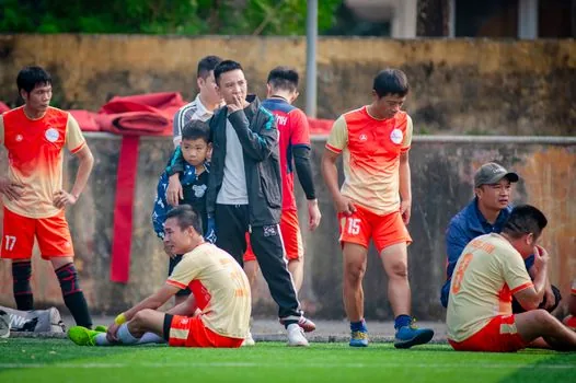 Vietnam national team training session with mixed squad players stretching near goalpost, Korean coach observing from sideline, realistic football photo, warm Hanoi evening light, no identifiable real faces | 베트남 대표팀 훈련에서 김상식 감독과 다양한 선수 구성을 함께 보여주는 장면
