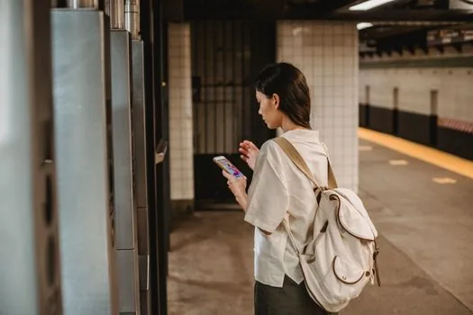 Korean commuter checking bus route app and alternative subway route on smartphone in shaded station area during heatwave, realistic editorial photo, no readable text