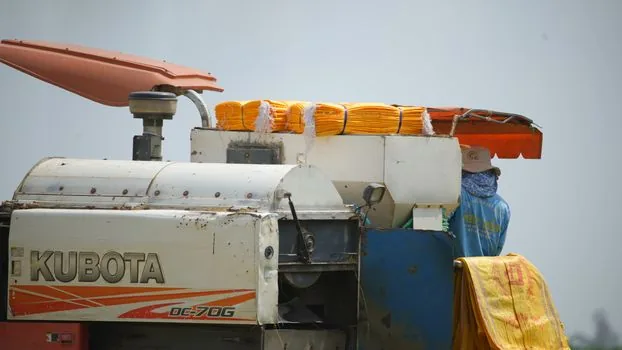 Korean field worker taking a short break in shade, drinking water, cooling towel around neck, summer outdoor worksite, realistic photo, no logos