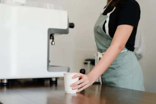 Korean person setting e-receipt option in shopping app while holding reusable tumbler at a cafe counter, bright lifestyle photo