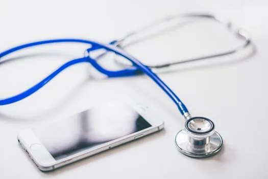 smartphone showing clinic search results beside handwritten call checklist and health insurance card, Korean public clinic reception mood, realistic bright photo | 위탁의료기관 검색 뒤 전화 확인할 항목을 적어두는 장면