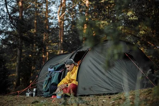 Camper reviewing reservation cancellation and refund status on laptop at home, camping backpack and folded tent nearby, realistic lifestyle photo