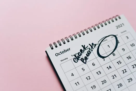 Close-up of calendar with even months marked for campsite lottery application, smartphone reservation page blurred, camping lantern and notebook on table, realistic photo