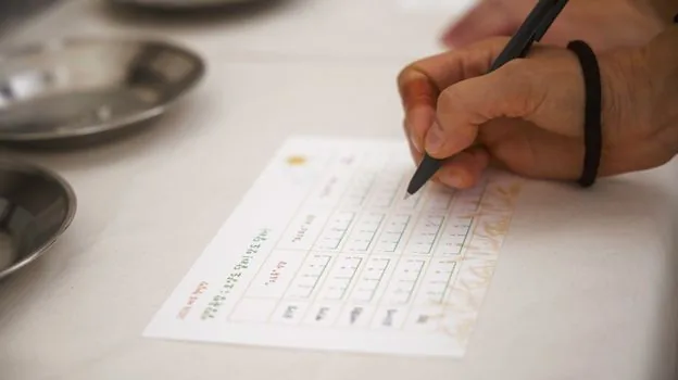close view of hands writing fainting symptoms time place trigger diary beside water bottle, realistic health checklist photo, no text | 실신 전조증상 시간과 상황을 기록하는 장면