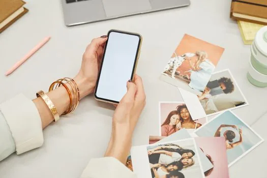 family member checking iCloud shared photo library options on phone before leaving shared library, laptop backup screen beside printed photos | iCloud 공유 사진 보관함을 나가기 전 보관 옵션을 확인하는 장면