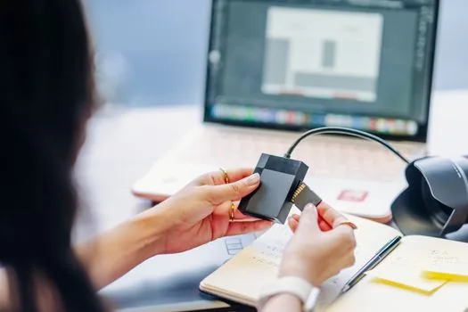 Korean adult checking certificate transfer page on laptop while holding smartphone with verification code, bright practical home desk, no private numbers readable | PC와 스마트폰을 함께 놓고 인증서 복사 방향을 확인하는 장면