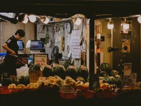 Korean convenience store counter with small over the counter medicine packages separated from food shelves, night lighting, realistic documentary photo, no readable logos