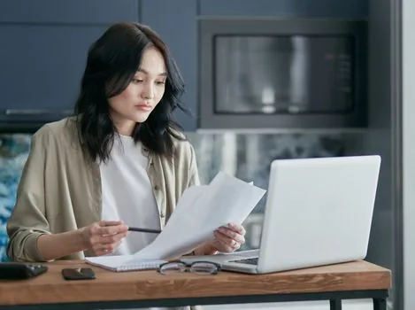 Korean driver checking unpaid traffic fine notice and safe driving pledge documents on kitchen table, realistic editorial photo no text