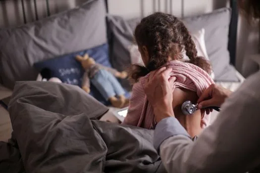 Korean parent checking child temperature while another adult searches open pediatric clinic on laptop and smartphone, night home setting, realistic photo