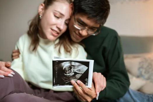 Korean parent reviewing Government24 Happy Birth support application with baby notebook, bankbook and checklist, bright home desk, realistic photo | 출생신고 뒤 행복출산 원스톱서비스 신청 항목을 확인하는 장면