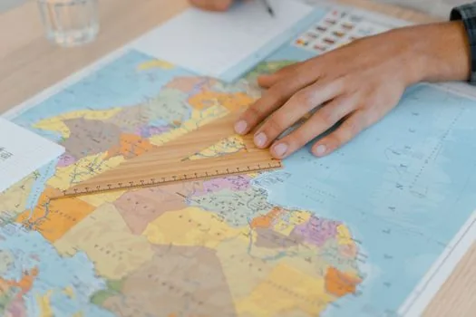 Korean person comparing cadastral map and land use planning document on laptop, muted map colors blurred, desk with ruler and checklist, realistic editorial photography | 토지대장과 토지이용계획 도면을 구분해 확인하는 장면