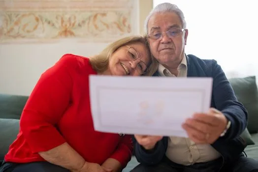 senior couple comparing housing options checklist, senior town brochure, law document tabs, and reading glasses on table